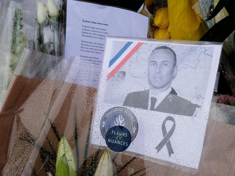 Blumen mit dem Portrait des bei einer Geiselnahme in Trébes getöteten Polizeibeamten Arnaud Beltrame liegen vor dessen Arbeitsplatz, der Gendarmerie in Carcassonne im Südwesten Frankreichs.