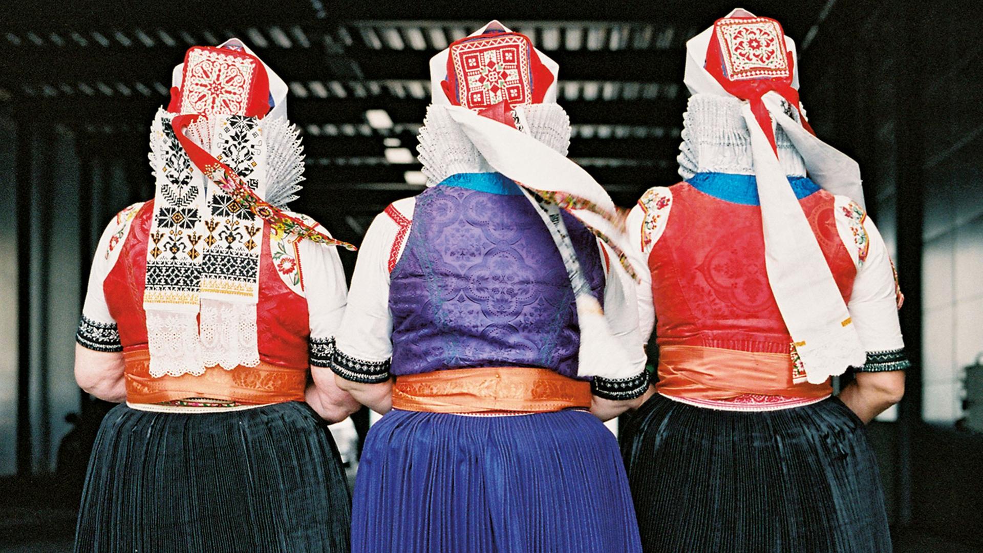 Rückansicht von drei alten Frauen in traditioneller Tracht, mit roten Hauben, weißen Spitzkragen und schwarzen oder blauen Röcken. Rückansicht von drei alten Frauen in traditioneller Tracht, mit roten Hauben, weißen Spitzkragen und schwarzen oder blauen Röcken.