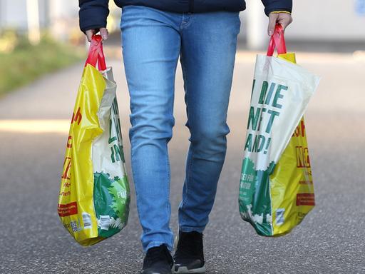 Zwei Hände tragen Plastiktüten.