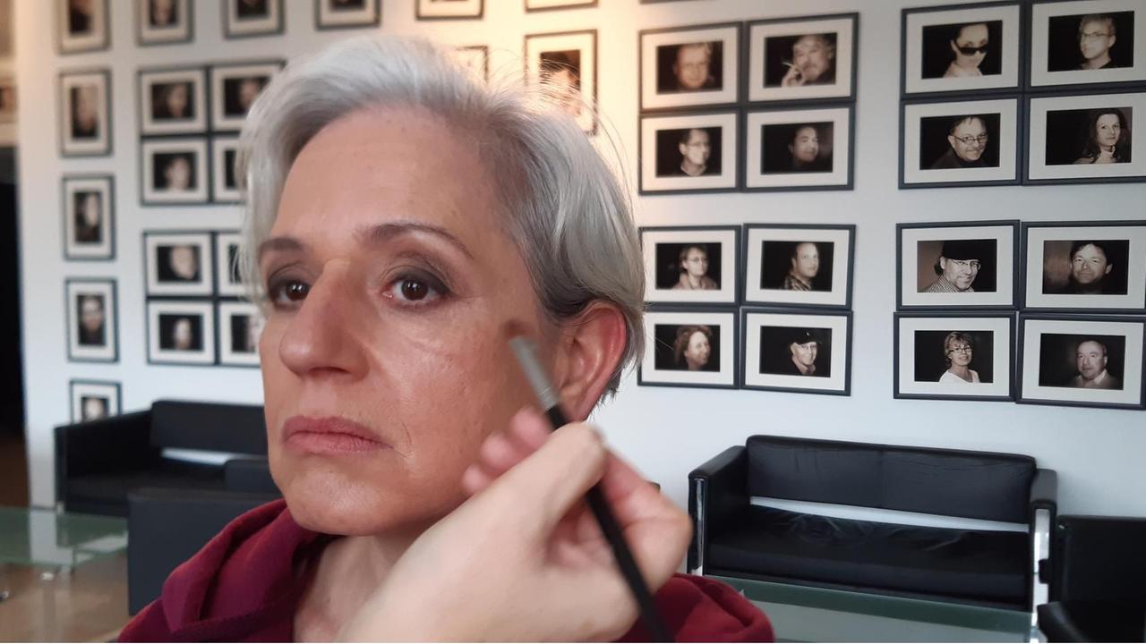 Vivian Kanner wird in der Maske für einen Fernsehauftritt. Sie tragt kurzte, graue Haare und schaut rechts an der Kamera vorbei. ´Mit einem Pinsel werden ihr Wangenknochen unterstrichen. Hinter ihr an der Wand hängen viele schwarz-weiß Portraits. Vivian Kanner wird in der Maske für einen Fernsehauftritt. Sie tragt kurzte, graue Haare und schaut rechts an der Kamera vorbei. ´Mit einem Pinsel werden ihr Wangenknochen unterstrichen. Hinter ihr an der Wand hängen viele schwarz-weiß Portraits.