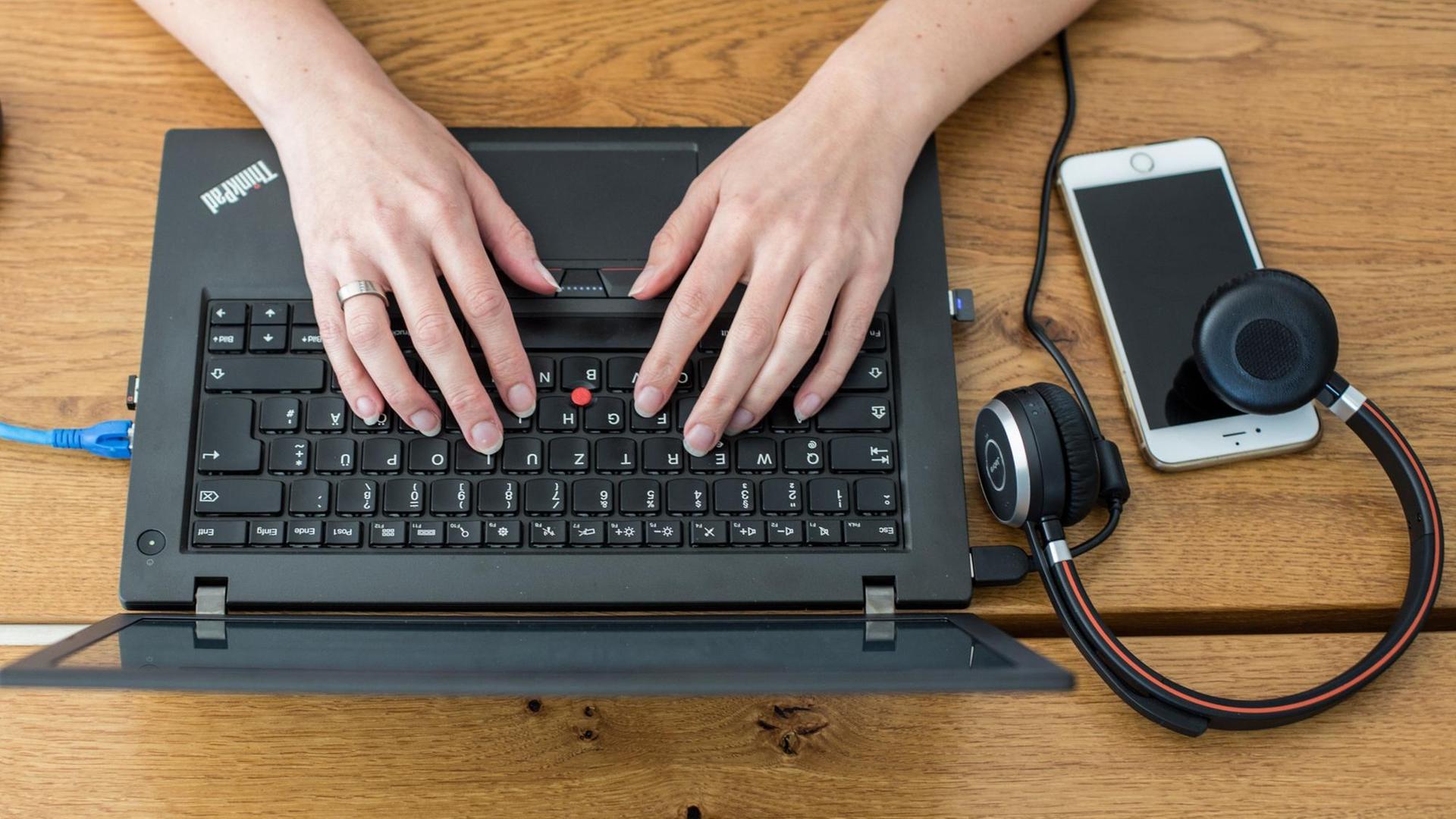 Das Foto zeigt zwei Hände, einen Computer, ein Handy und Kopfhörer, alles von oben. Das Foto zeigt zwei Hände, einen Computer, ein Handy und Kopfhörer, alles von oben.