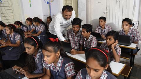 Das Foto zeigt eine öffentliche Schule in Ahmedabad/Indien im Juli 2018. Ein Lehrer erläutert den Schülerinnen und Schülern die Computer-Arbeit im E-Klassenraum.