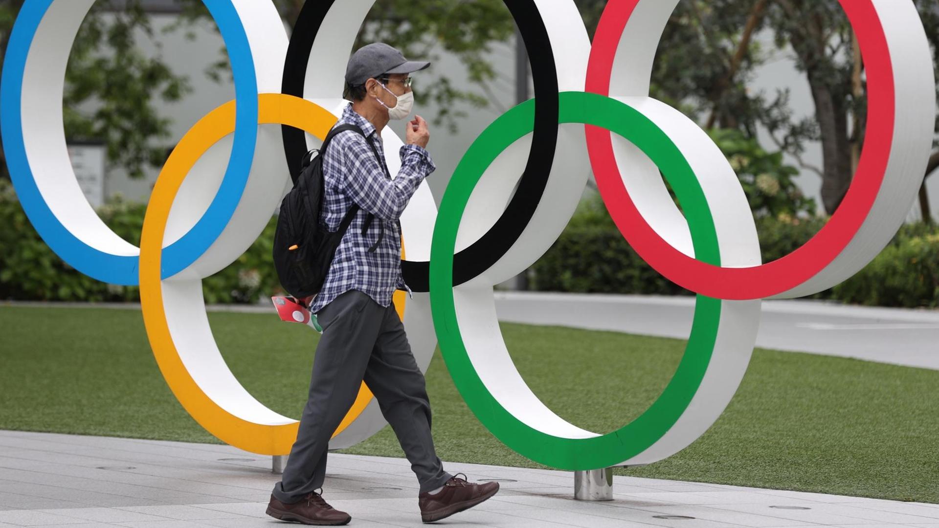 Ein Mann mit Maske läuft an einer Installation Olympischer Ringe vorbei, die in Tokio an die wegen Corona verschobene Sportveranstaltung erinnert. Ein Mann mit Maske läuft an einer Installation Olympischer Ringe vorbei, die in Tokio an die wegen Corona verschobene Sportveranstaltung erinnert.