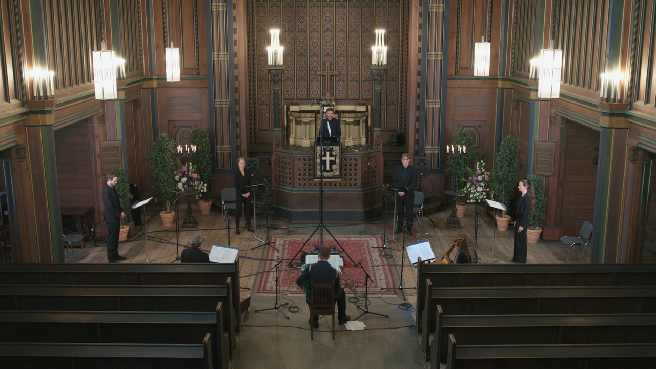 Vier Sänger und vier Musiker sitzen und stehen in einem großen Kreis im Altarbereich.