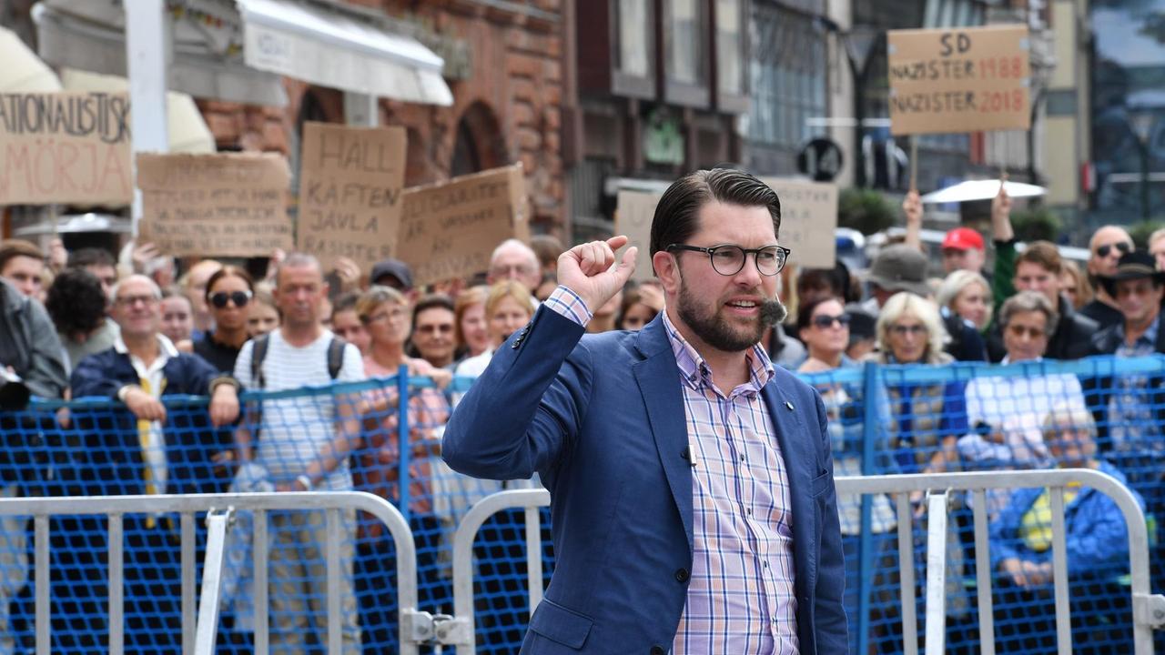 Der Vorsitzende der rechtspopulistischen Schwedendemokraten: Jimmie Åkesson bei einer Veranstaltung im August 2018. Im Hintergrund Demonstranten. Der Vorsitzende der rechtspopulistischen Schwedendemokraten: Jimmie Åkesson bei einer Veranstaltung im August 2018. Im Hintergrund Demonstranten.