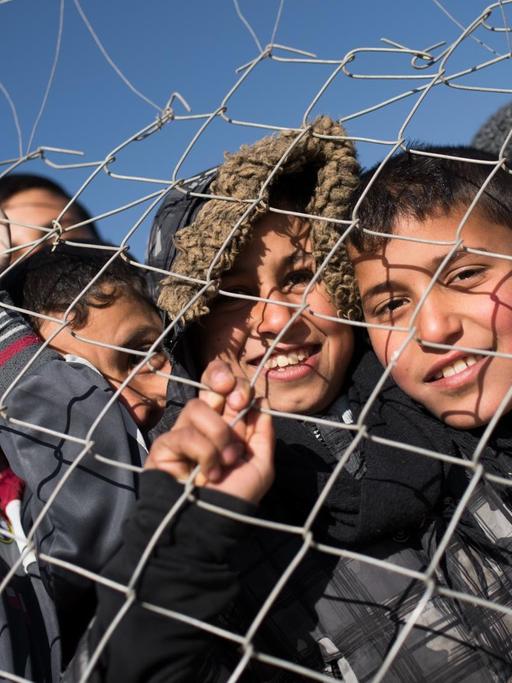 Flüchtlingskinder stehen an einem Zaun.