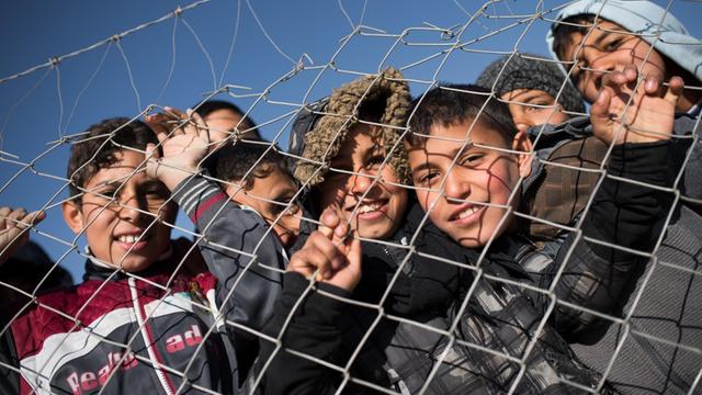 Flüchtlingskinder stehen an einem Zaun.