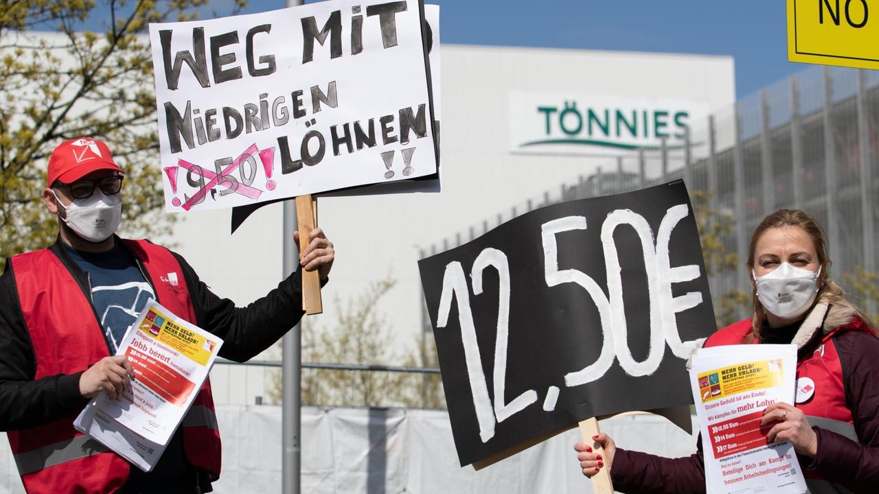 "Weg mit niedrigen Löhnen!" und "12,50 €" steht auf Plakaten, die ein Gewerkschaftsvertreter und eine Gewerkschaftsvertreterin in der Hand halten. Mit der Aktion wird vor dem Werk von Tönnies für höhere Löhne protestiert. "Weg mit niedrigen Löhnen!" und "12,50 €" steht auf Plakaten, die ein Gewerkschaftsvertreter und eine Gewerkschaftsvertreterin in der Hand halten. Mit der Aktion wird vor dem Werk von Tönnies für höhere Löhne protestiert.