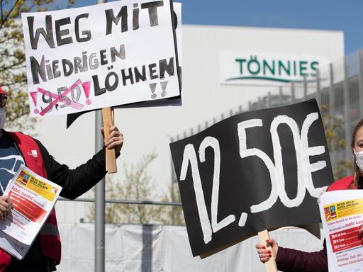 "Weg mit niedrigen Löhnen!" und "12,50 €" steht auf Plakaten, die ein Gewerkschaftsvertreter und eine Gewerkschaftsvertreterin in der Hand halten. Mit der Aktion wird vor dem Werk von Tönnies für höhere Löhne protestiert.