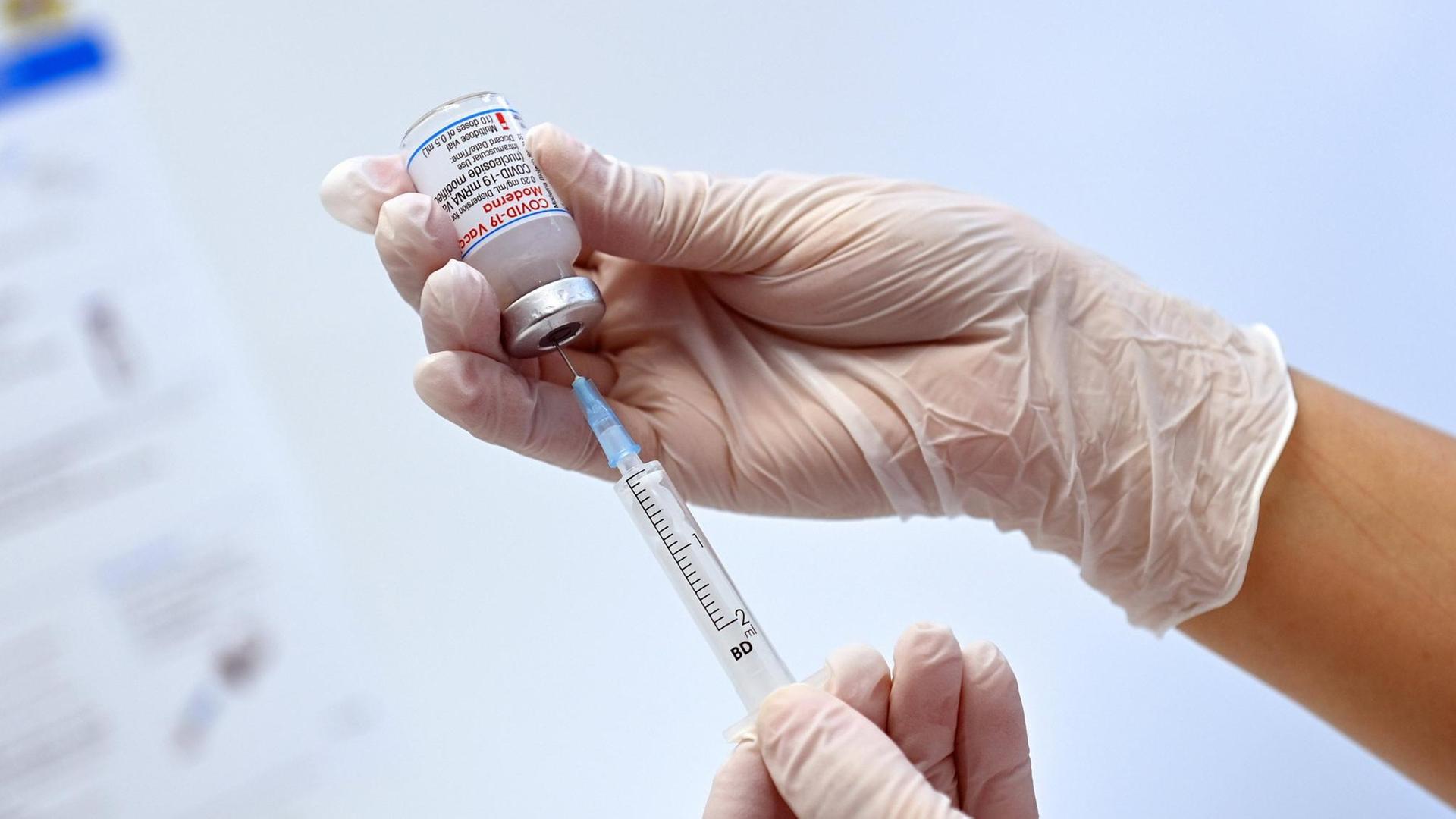 Eine Hand hält eine Impfdose mit dem Moderna mRnA-Impfstoff und zieht ihn mit einer Spritze heraus