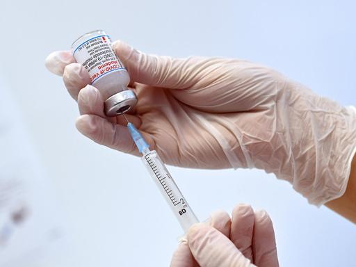 Eine Hand hält eine Impfdose mit dem Moderna mRnA-Impfstoff und zieht ihn mit einer Spritze heraus