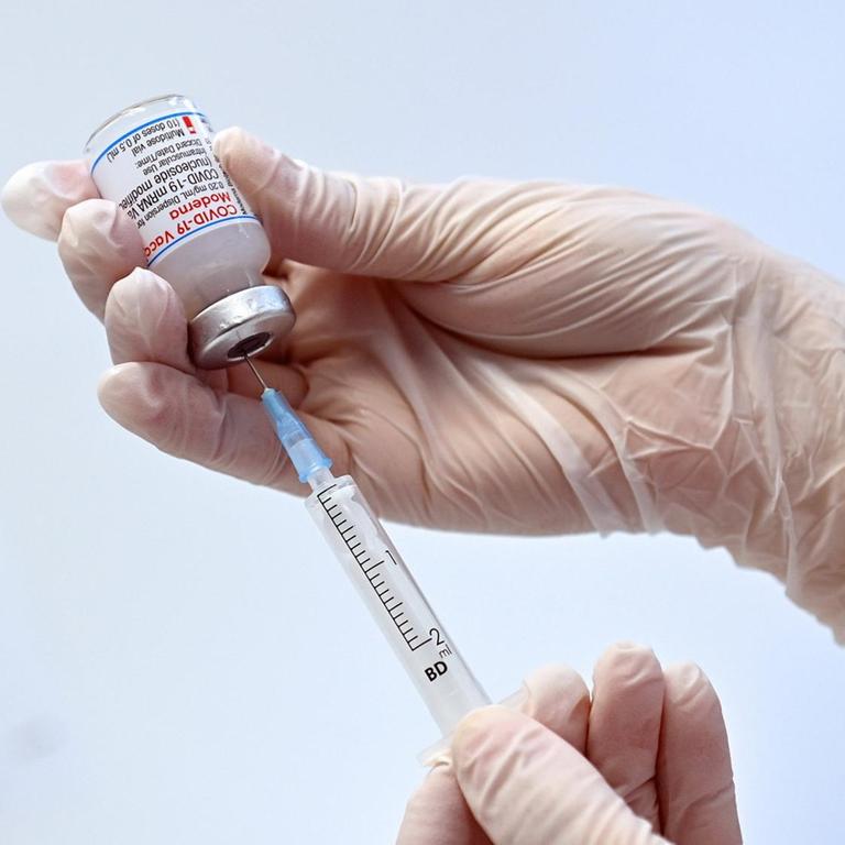 A hand holds a vaccine box with the Moderna mRnA vaccine and pulls it out with a syringe, pictured June 23, 2021 at the Freising Vaccination Center