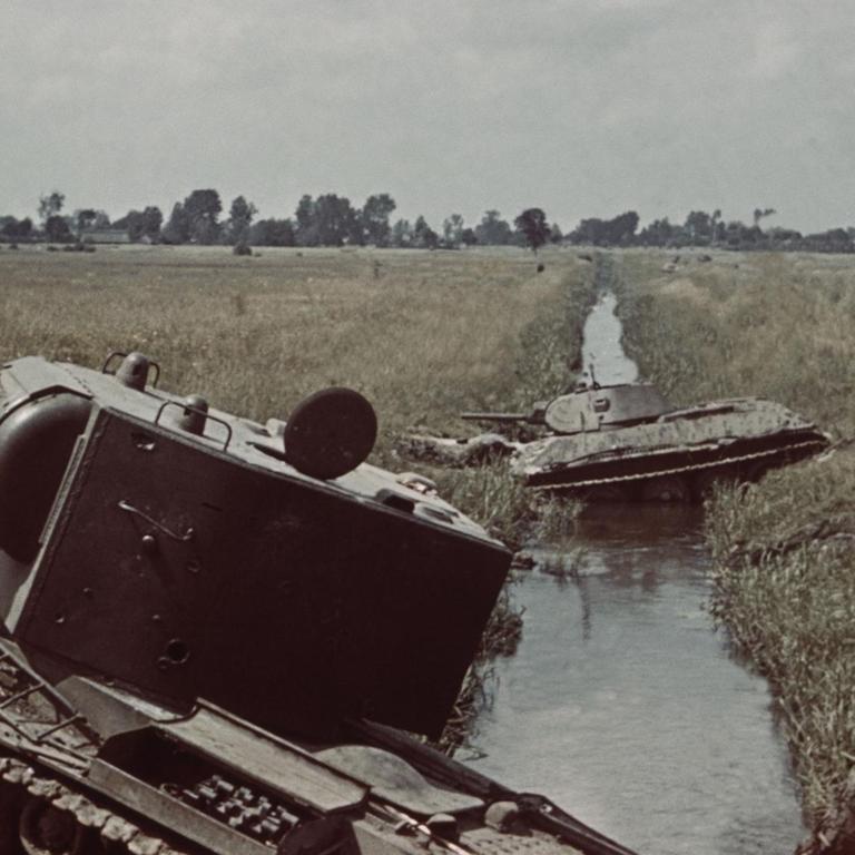 Ein historisches Farbfoto zeigt die Trümmer zweier Panzer an der Böschung eines Kanals