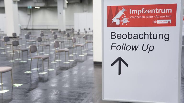 Blick in den Wartebereich des Impfzentrums in Köln. Zu sehen ist ein Schild mit der Aufschrift "Impfzentrum" und viele leere Stühle, die auf Abstand zueinander aufgestellt sind. Blick in den Wartebereich des Impfzentrums in Köln. Zu sehen ist ein Schild mit der Aufschrift "Impfzentrum" und viele leere Stühle, die auf Abstand zueinander aufgestellt sind.