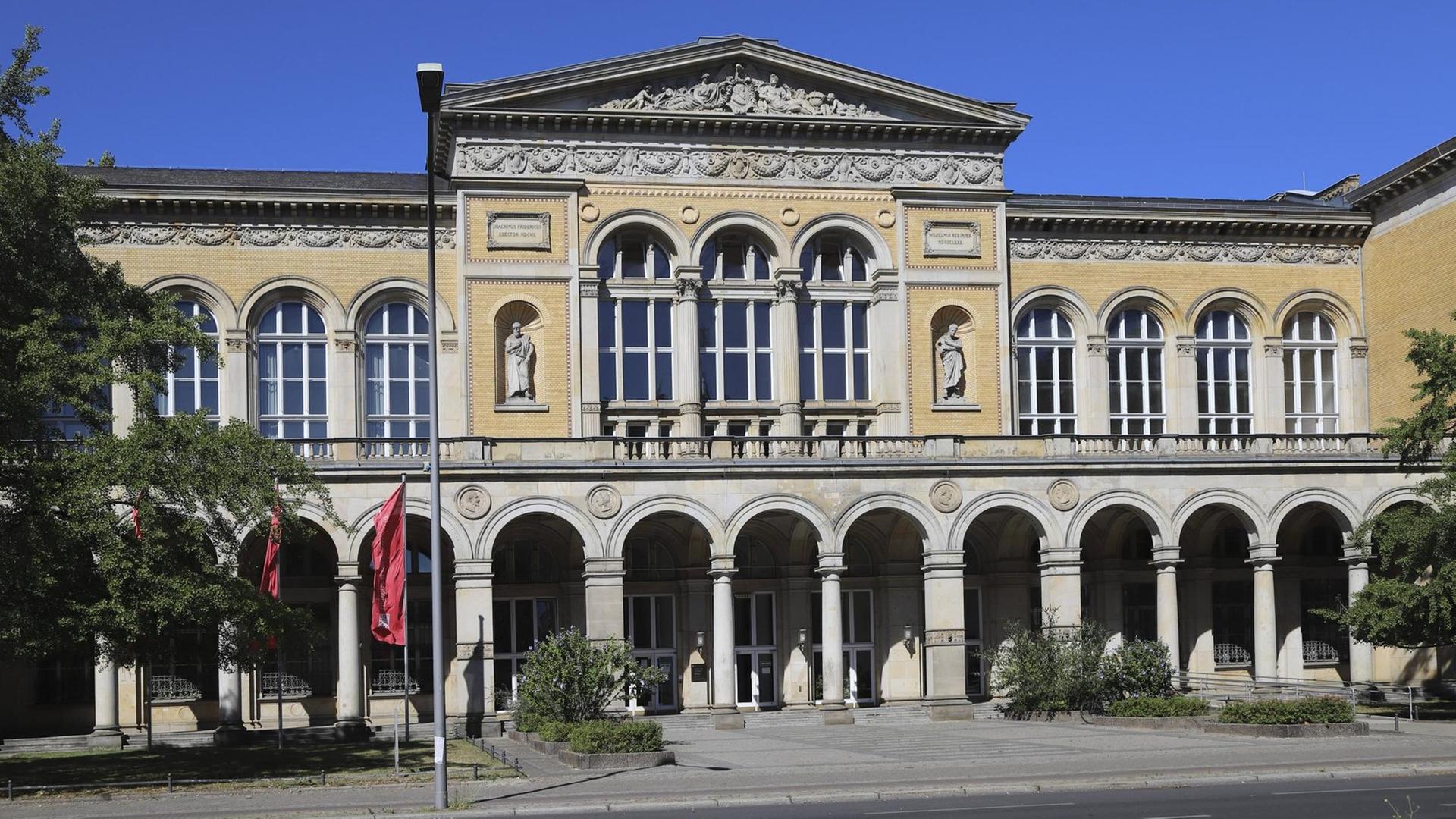 Vor dem stattlischen Eingang mit Säulenmotiven eines historischen Gebäudes wehen Fahnen mit dem Schriftzug der UdK Berlin. Vor dem stattlischen Eingang mit Säulenmotiven eines historischen Gebäudes wehen Fahnen mit dem Schriftzug der UdK Berlin.