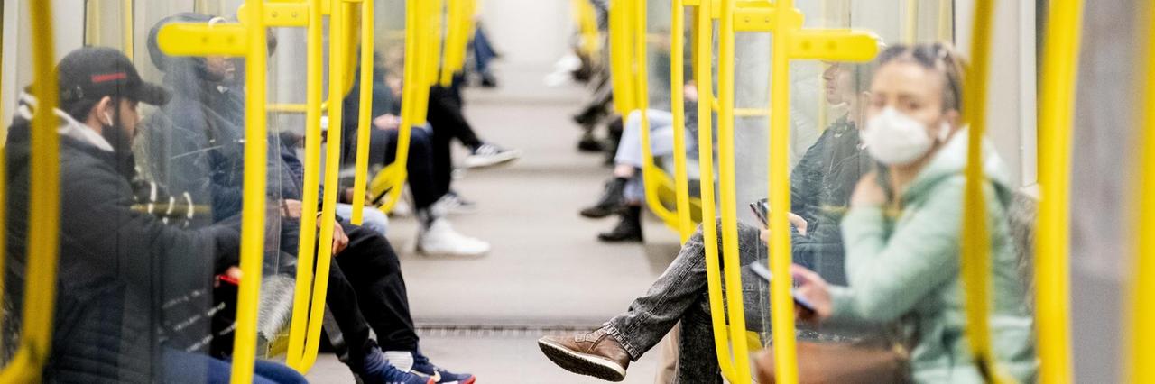 Fahrgäste sitzen in einer U-Bahn, wobei eine Frau einen Mundschutz trägt. Fahrgäste sitzen in einer U-Bahn, wobei eine Frau einen Mundschutz trägt.