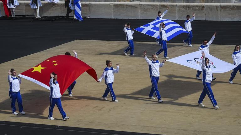 Delegationen tragen die Flaggen Chinas, (vorn l), Griechenlands, Chinas und die Olympische Flagge (r) während der Zeremonie zur Übergabe der Flamme für die Olympischen Winterspiele 2022 im Panathenäischen Stadion. Die Olympischen Winterspiele finden vom 4. bis 20. Februar 2022 in Peking statt.