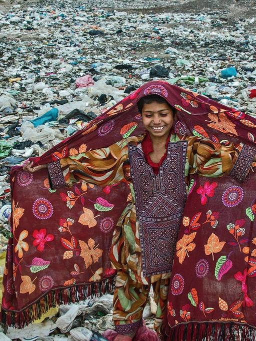 Das Foto des Jahres: Es zeigt ein lächelndes Mädchen. Das Mädchen hat bunte Kleidung. Es steht auf einem Berg von Müll.