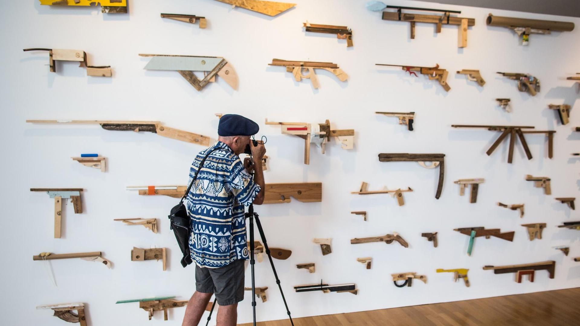 Ein Fotograf lichtet in der Ausstellung "Unter Waffen. Fire & Forget 2" eine Installtion von "Robbert&Frank Frank&Robbert" ab, die 95 hauptsächlich in Holz nachgebildete Waffen an einer Wand beinhaltet. Ein Fotograf lichtet in der Ausstellung "Unter Waffen. Fire & Forget 2" eine Installtion von "Robbert&Frank Frank&Robbert" ab, die 95 hauptsächlich in Holz nachgebildete Waffen an einer Wand beinhaltet.
