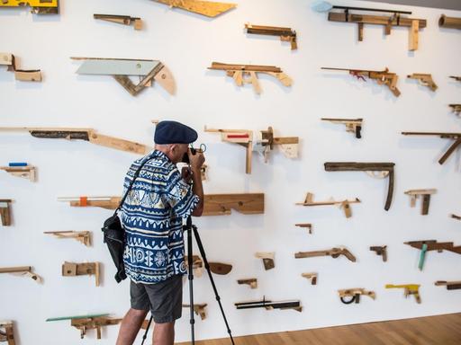 Ein Fotograf lichtet in der Ausstellung "Unter Waffen. Fire & Forget 2" eine Installtion von "Robbert&Frank Frank&Robbert" ab, die 95 hauptsächlich in Holz nachgebildete Waffen an einer Wand beinhaltet.