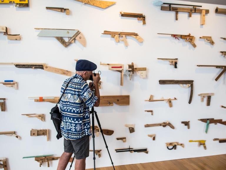 Ein Fotograf lichtet in der Ausstellung "Unter Waffen. Fire & Forget 2" eine Installtion von "Robbert&Frank Frank&Robbert" ab, die 95 hauptsächlich in Holz nachgebildete Waffen an einer Wand beinhaltet.