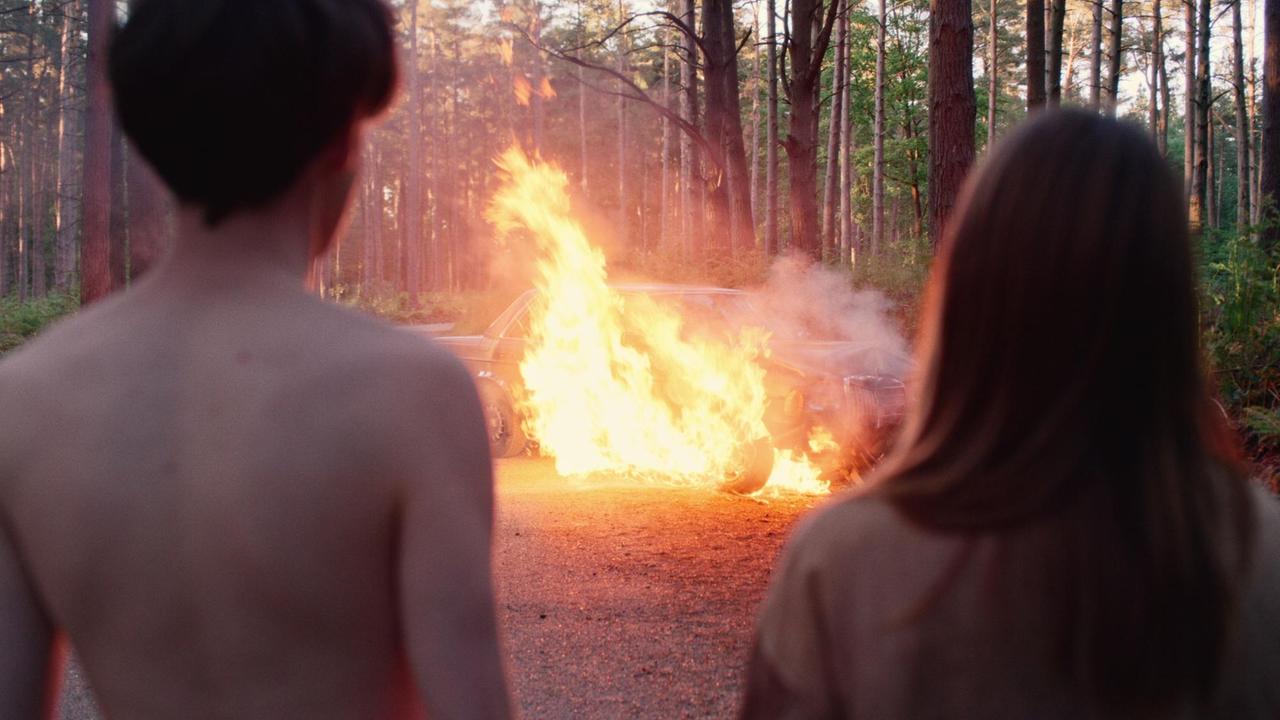 Ausschnitt aus der Serie "The End of the F***ing World" : Alyssa und James stehen vor einem brennenden Auto. Ausschnitt aus der Serie "The End of the F***ing World" : Alyssa und James stehen vor einem brennenden Auto.