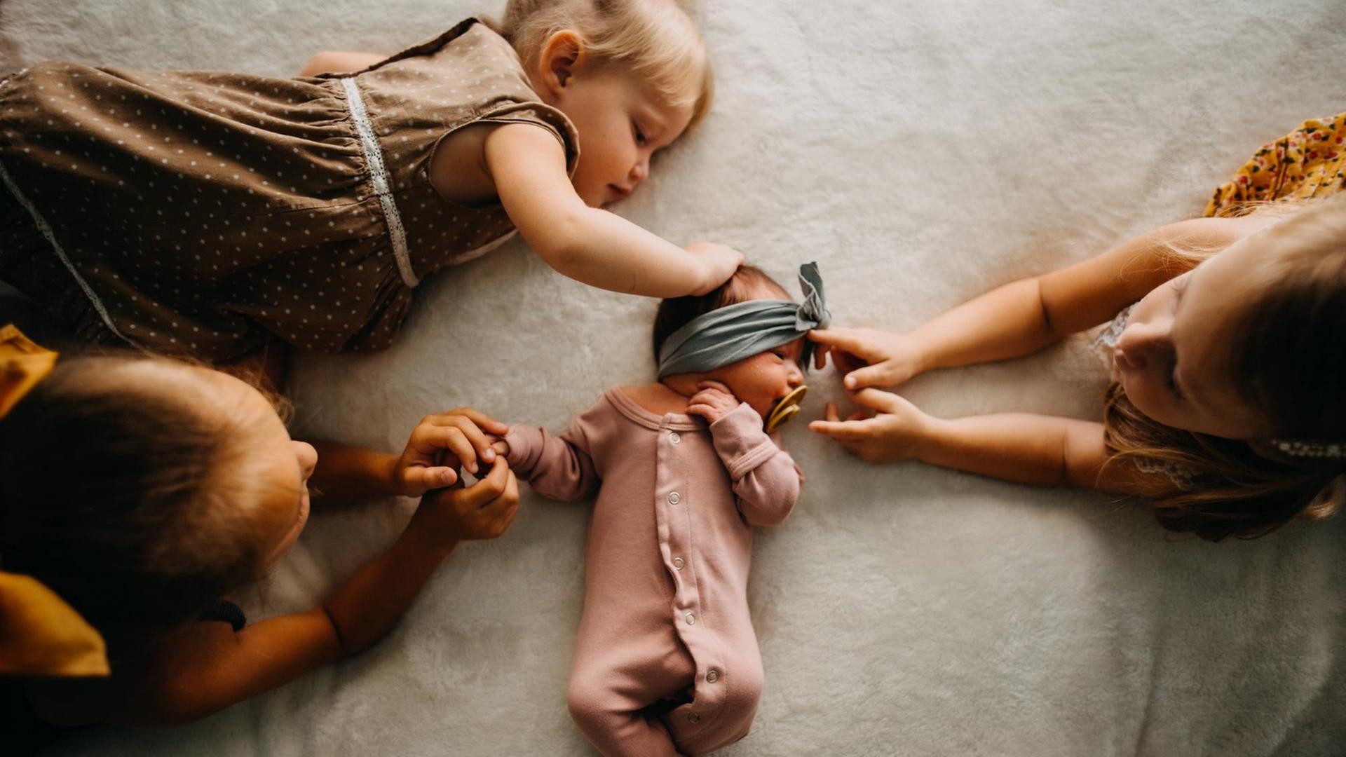 Drei Schwestern berühren ein kleines Baby in ihrer Mitte Drei Schwestern berühren ein kleines Baby in ihrer Mitte