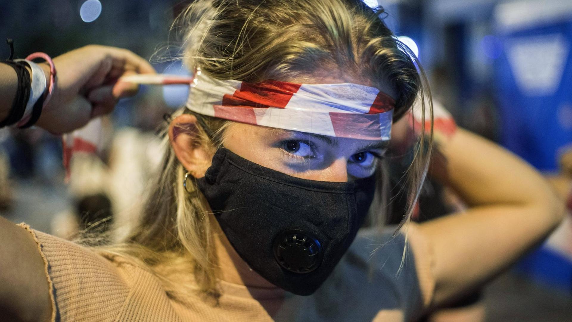 Demonstrantin in Budapest wickelt sich rot-weißes Flatterband um den Kopf. Demonstrantin in Budapest wickelt sich rot-weißes Flatterband um den Kopf.