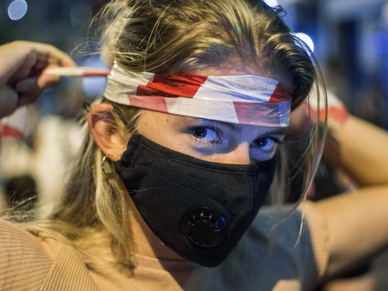 Demonstrantin in Budapest wickelt sich rot-weißes Flatterband um den Kopf.