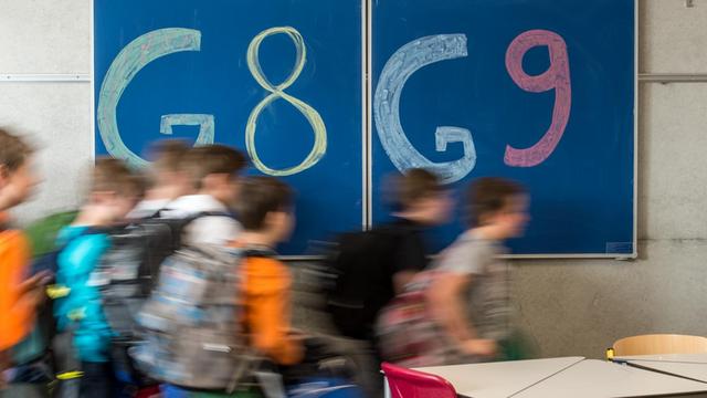 Kinder gehen in einem Klassenzimmer eines Gymnasiums in Straubing (Bayern) an einer Tafel vorbei, auf der "G8" und "G9" steht.