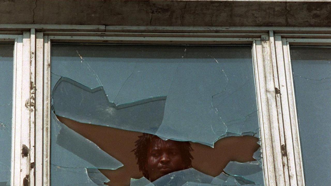 Ein Asylbewerber schaut am 23.9.1991 aus einem eingeschlagenen Fenster des Asylbewerberheims im sächsischen Hoyerswerda Ein Asylbewerber schaut am 23.9.1991 aus einem eingeschlagenen Fenster des Asylbewerberheims im sächsischen Hoyerswerda