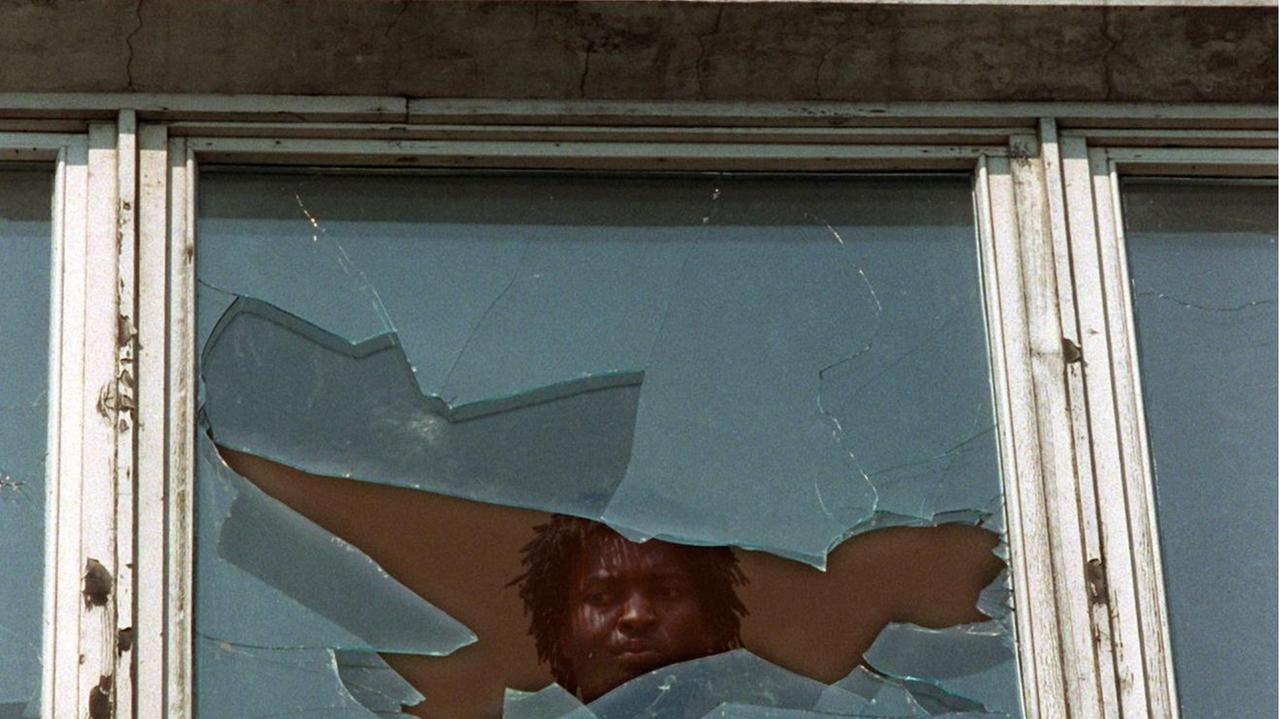 Ein Asylbewerber schaut am 23.9.1991 aus einem eingeschlagenen Fenster des Asylbewerberheims im sächsischen Hoyerswerda Ein Asylbewerber schaut am 23.9.1991 aus einem eingeschlagenen Fenster des Asylbewerberheims im sächsischen Hoyerswerda