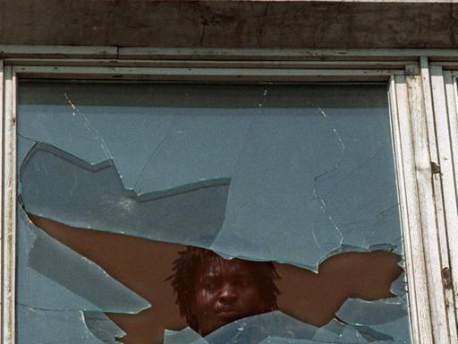 Ein Asylbewerber schaut am 23.9.1991 aus einem eingeschlagenen Fenster des Asylbewerberheims im sächsischen Hoyerswerda