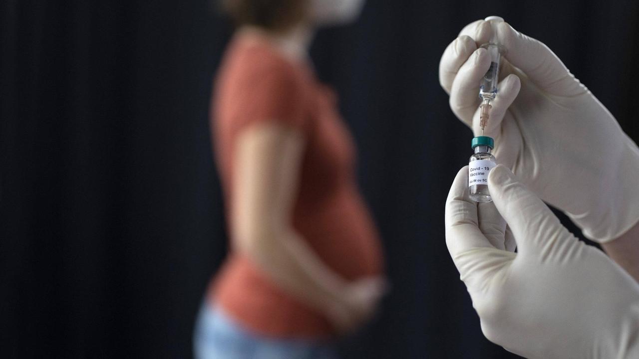 Eine Schwangere hält sich den Bauch; im Vordergrund sind zwei Hände zu sehen, die Impfstoff aus einer Dose in eine Spritze ziehen. (Symboldbild)