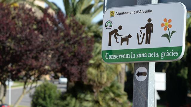 Ein Schild fordert zu Rücksicht und Sauberkeit auf, fotografiert am 05.05.2016 in Alcudia im Norden von Mallorca (Spanien). Im Hintergrund Mülltonnen für die Mülltrennung.