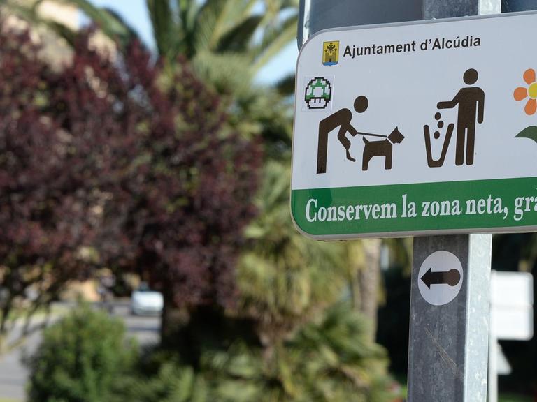Ein Schild fordert zu Rücksicht und Sauberkeit auf, fotografiert am 05.05.2016 in Alcudia im Norden von Mallorca (Spanien). Im Hintergrund Mülltonnen für die Mülltrennung.