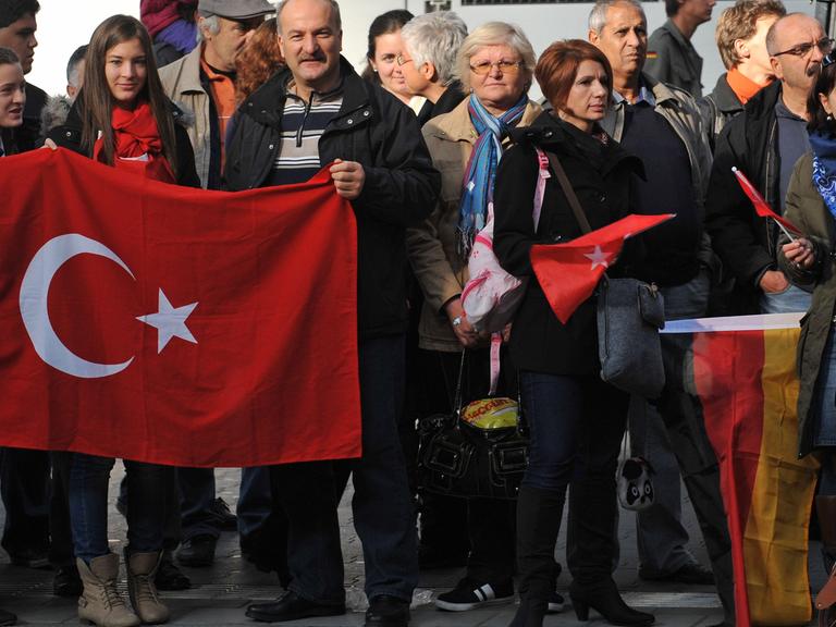 Menschen mit türkischen und deutschen Flaggen warten im Hauptbahnhof in München auf die Ankunft des Erinnerungszuges "50 Jahre Migration".