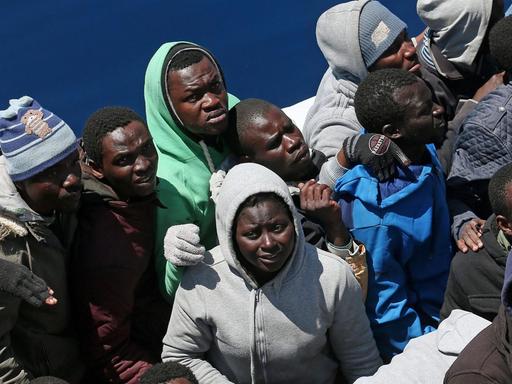Ein Dutzend Flüchtlinge drängen sich auf einem kleinen Boot im Mittelmeer, bevor sie auf das Schiff der Küstenwache gelangen können.