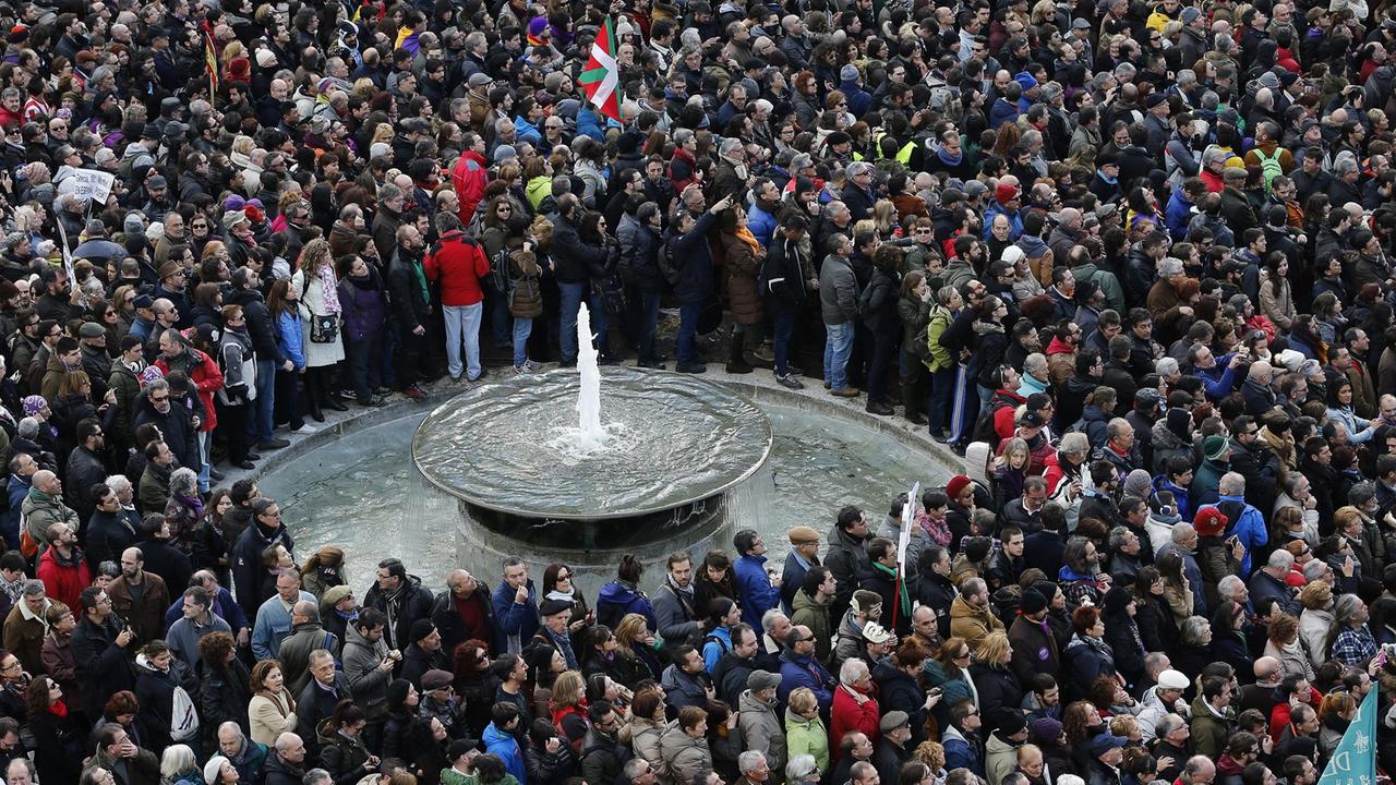 Dicht gedrängt stehen Menschen auf einem Platz, in ihrer Mitte ein Brunnen. Dicht gedrängt stehen Menschen auf einem Platz, in ihrer Mitte ein Brunnen.