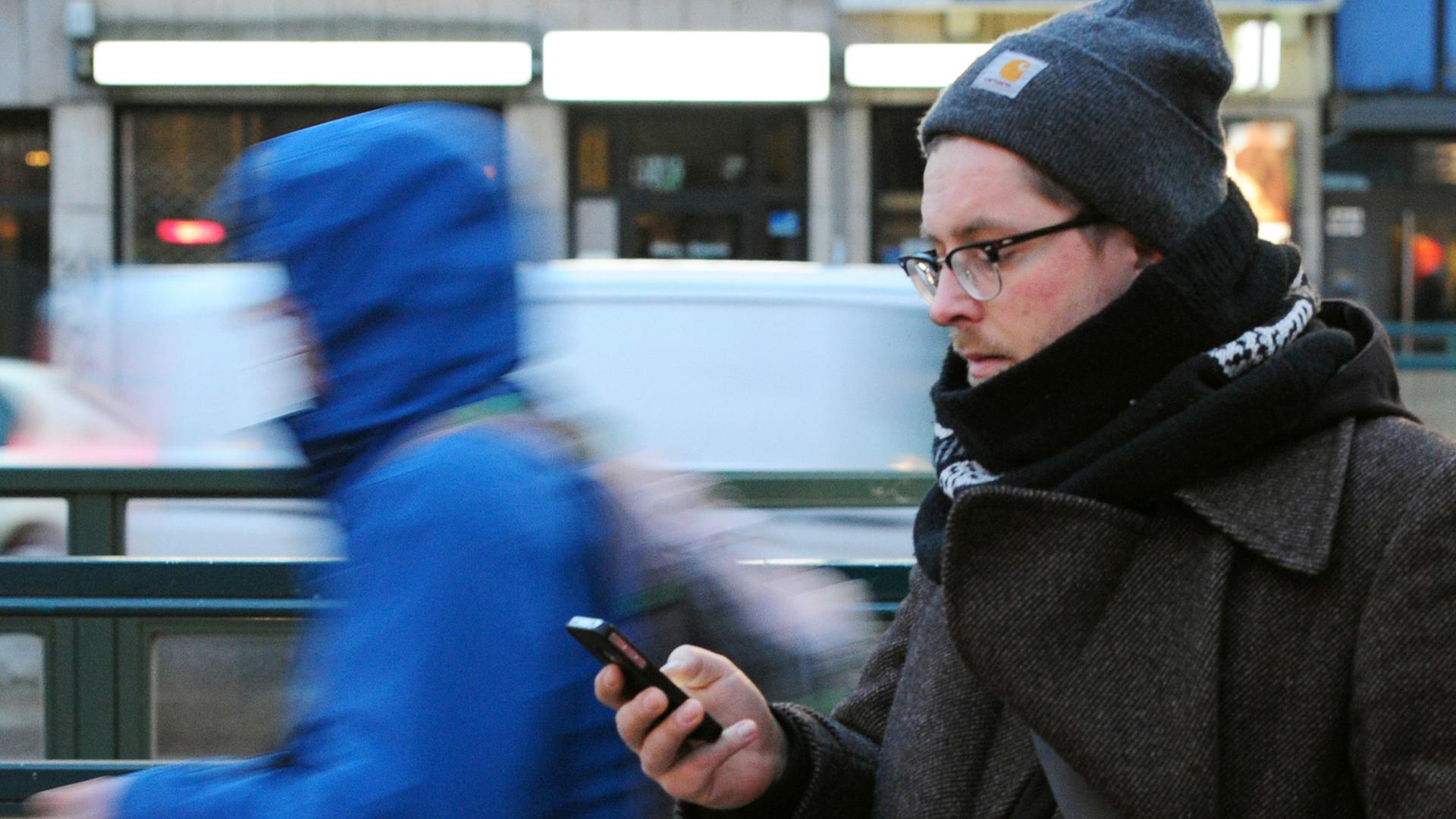 Ein junger Mann geht mit dem Blick auf sein Smartphone gerichtet. Ein junger Mann geht mit dem Blick auf sein Smartphone gerichtet.