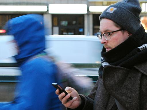Ein junger Mann geht mit dem Blick auf sein Smartphone gerichtet.