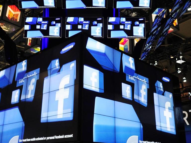 Das Facebook Logo ist auf zahlreichen Bildschirmen auf einem Messestand zu sehen.