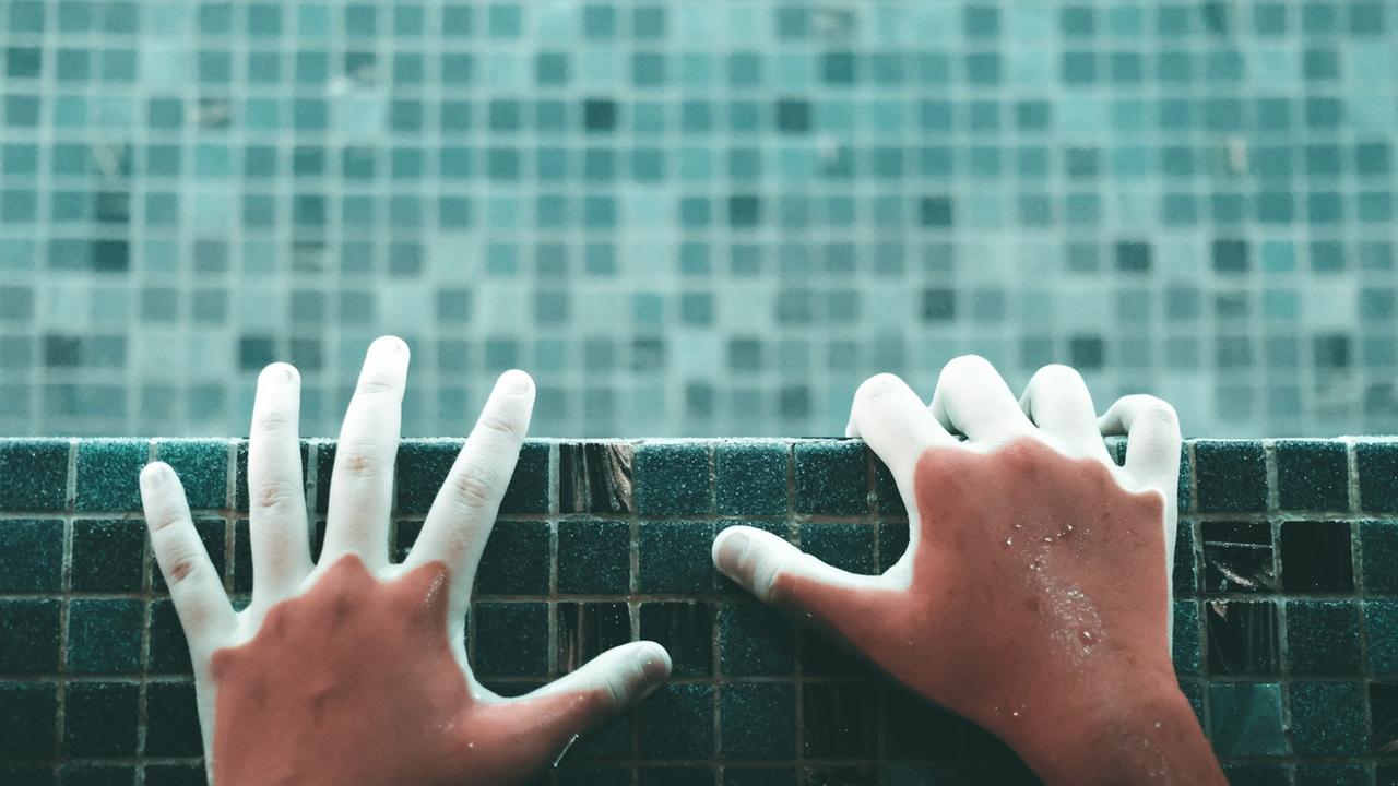Hände an einem Beckenrand eines Schwimmbeckens Hände an einem Beckenrand eines Schwimmbeckens