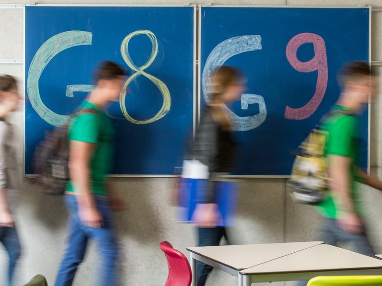 Schüler gehen an einer Tafel vorbei, auf der "G8" und "G9" steht.