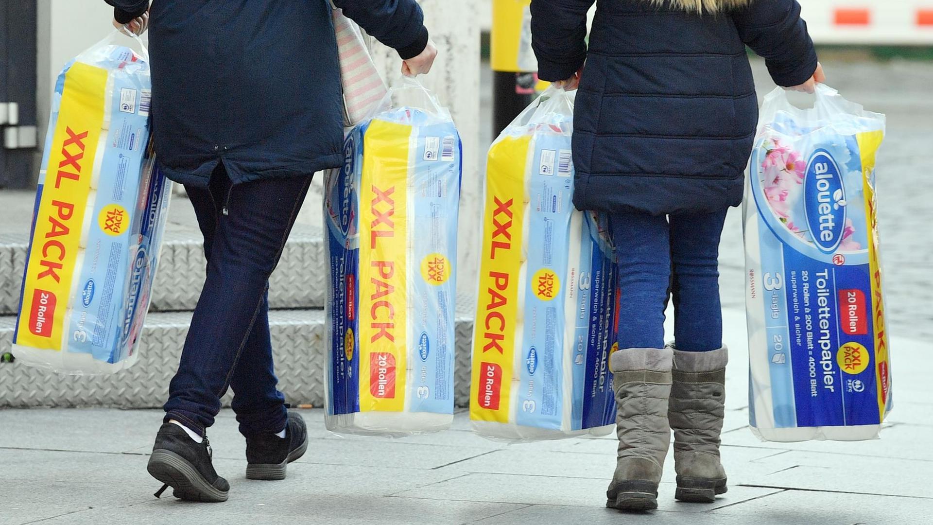 Menschen tragen mehrere Packungen Toilettenpapier aus einem Supermarkt.