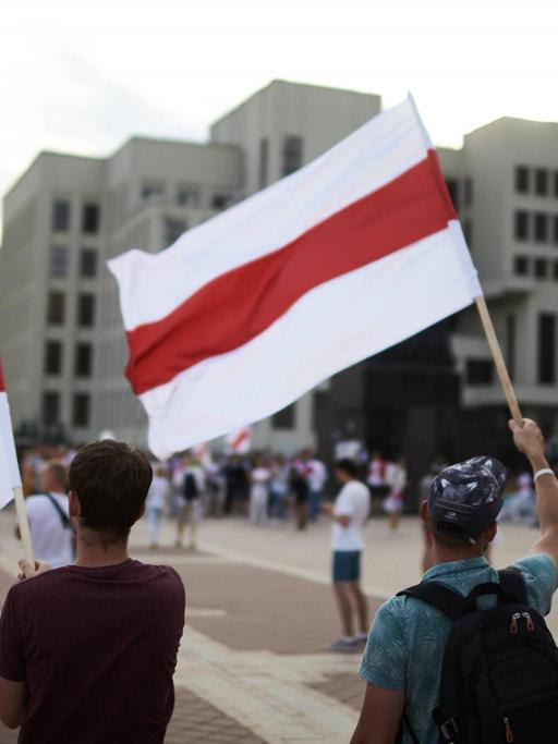Demonstranten stehen mit weiß-rot-weißen Flaggen auf einem Platz in Minsk