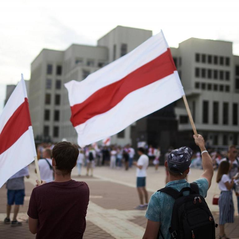 Demonstranten stehen mit weiß-rot-weißen Flaggen auf einem Platz in Minsk 