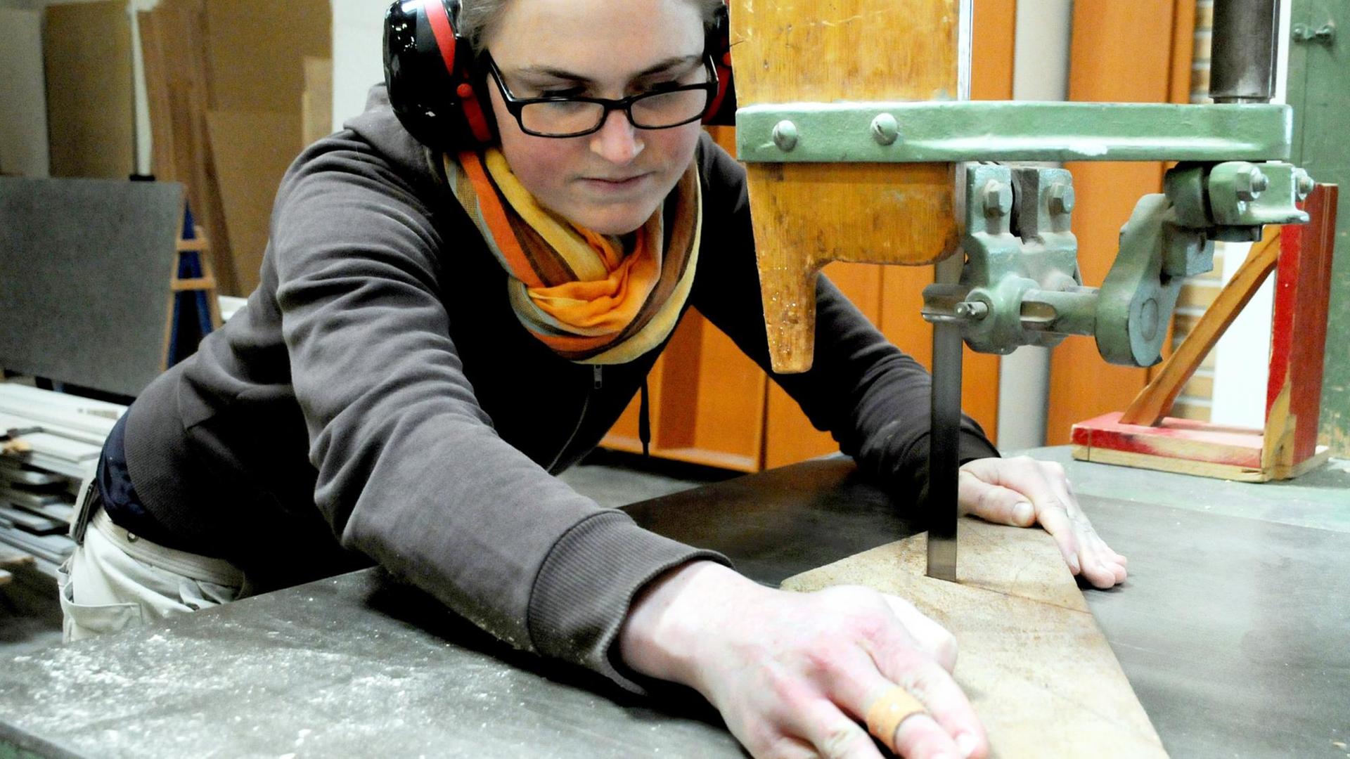 Eine Tischlerin schneidet ein Stück Holz zu. Eine Tischlerin schneidet ein Stück Holz zu.