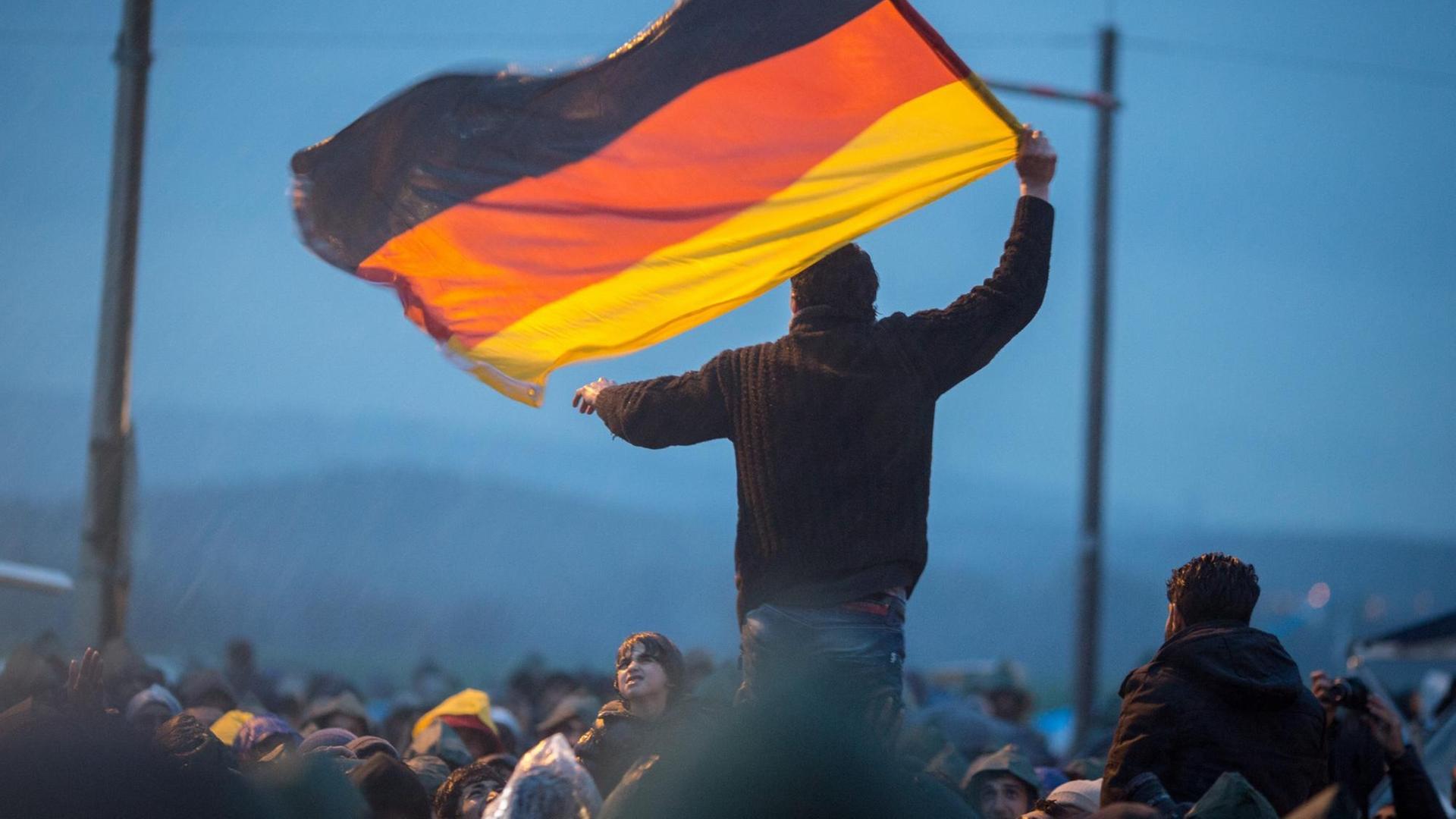 Ein Flüchtling schwent eine Deutschlandfahne in Idomeni an der Grenze zwischen Griechenland und Mazedonien. Ein Flüchtling schwent eine Deutschlandfahne in Idomeni an der Grenze zwischen Griechenland und Mazedonien.