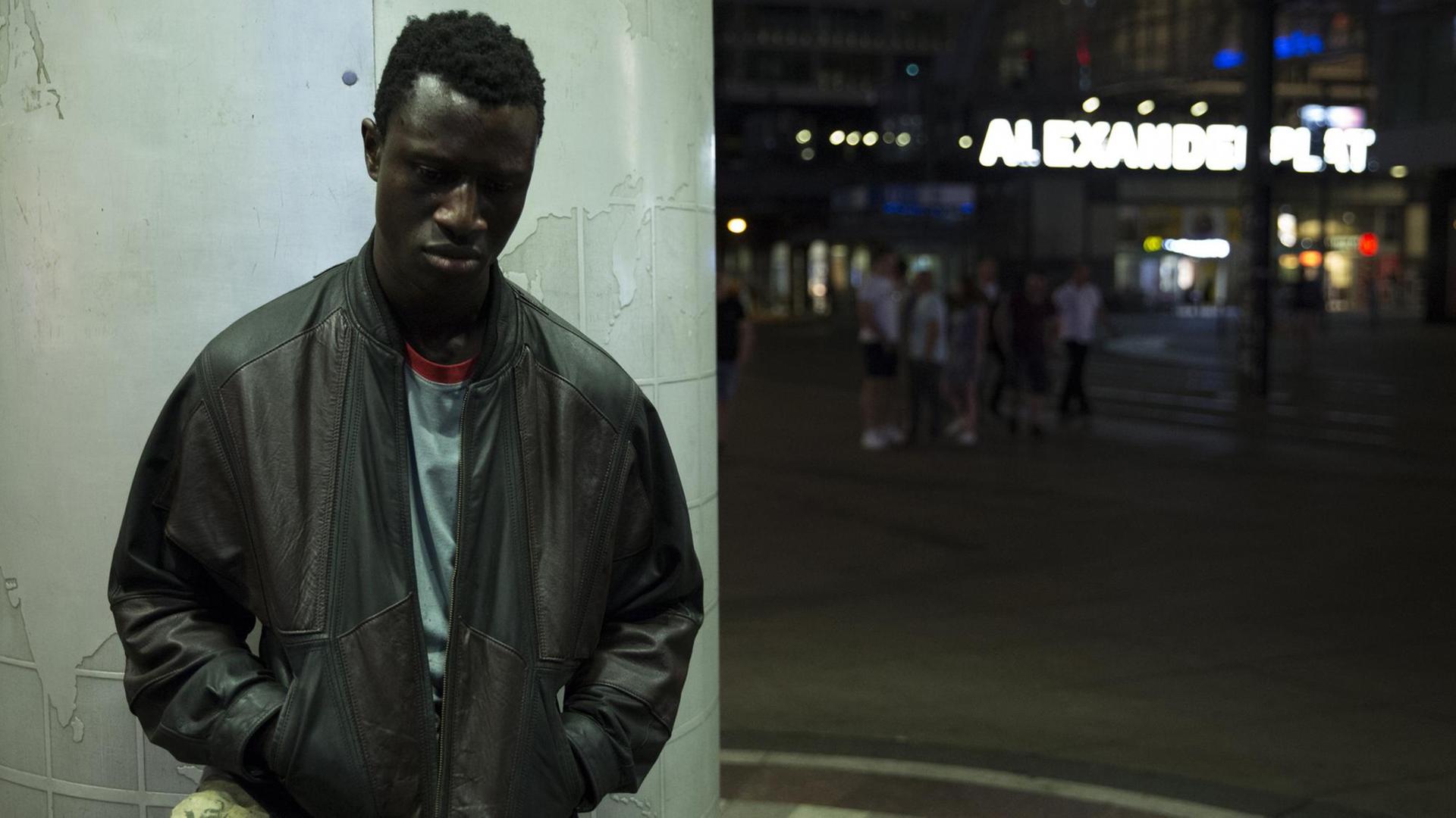 Der Schauspieler Welket Bungué steht im Film "Berlin Alexanderplatz" vor einer Säule, im Hintergrund der Neon-Schriftzug Alexanderplatz. Der Schauspieler Welket Bungué steht im Film "Berlin Alexanderplatz" vor einer Säule, im Hintergrund der Neon-Schriftzug Alexanderplatz.